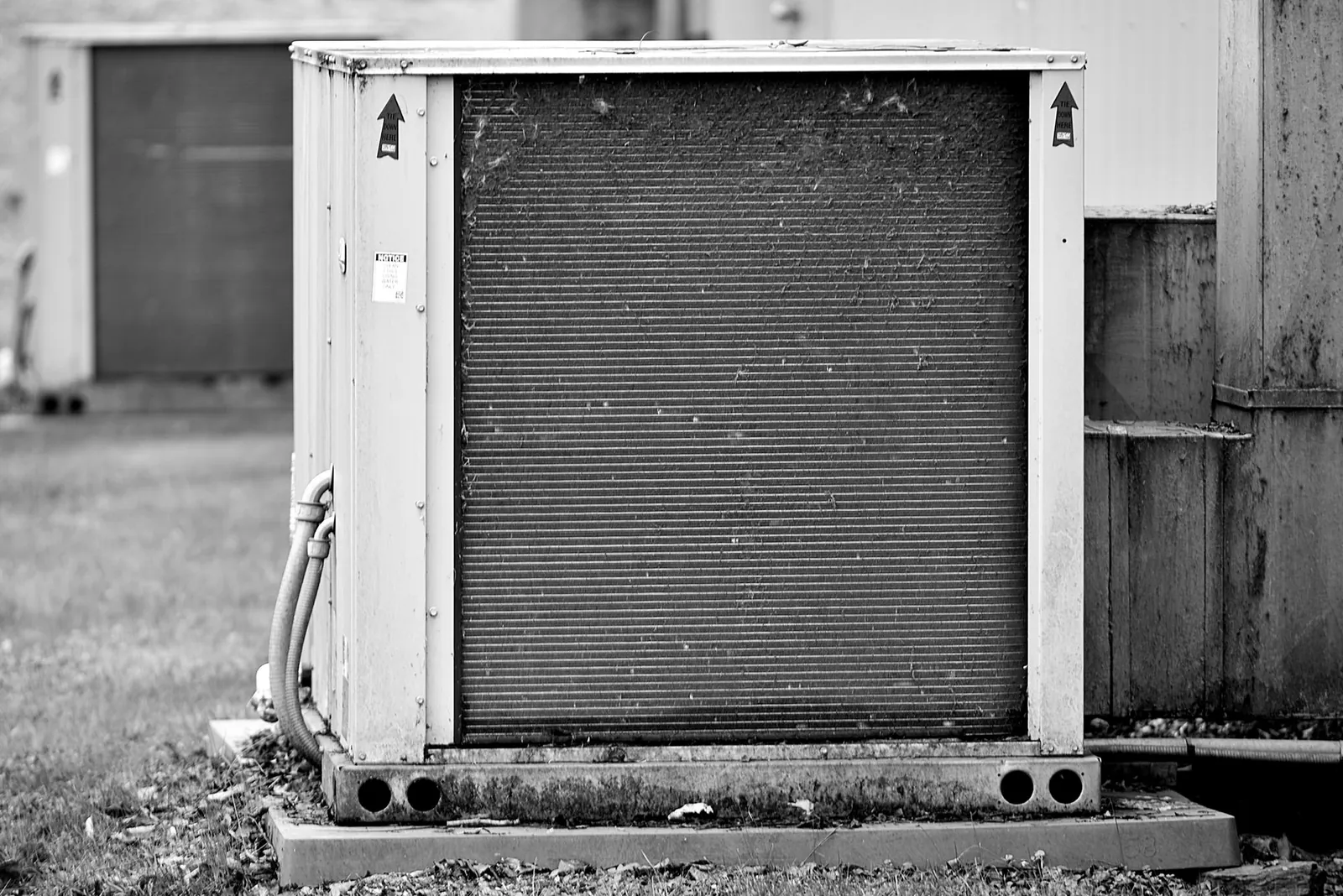 Weathered outdoor condensing unit with a dirty coil on a concrete pad beside a building